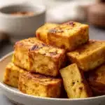 Close-up of crispy air fryer tofu with a golden brown texture on a clean white plate.
