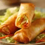 Close-up of crispy chicken spring rolls on a clean white plate with a dipping sauce.