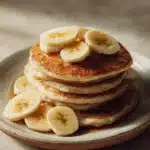 Close-up of fluffy banana pancakes stacked with syrup drizzling down.