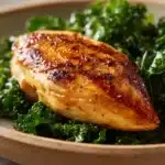 Close-up of grilled chicken breast with fresh kale on a white plate
