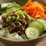 Close-up of a Korean ground beef bowl with rice and vegetables in warm lighting.