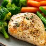 Close-up of a low calorie chicken dinner with creamy sauce and herbs on a white plate.