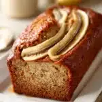 Close-up of a slice of maple banana bread with a golden crust on a clean white plate.