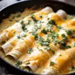 Close-up of skillet creamy chicken enchiladas with melted cheese and herbs