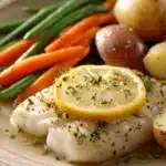 Close-up of a white fish dinner with lemon slices and herbs on a clean plate.