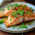 Close-up of air fryer salmon with ginger garnished with herbs on a white plate
