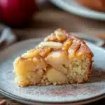 Close-up of a delicious apple cake slice with a golden crust and visible apple pieces.