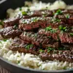 Close-up of honey butter garlic steak and rice skillet with herbs and garlic.