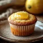 Close-up of a lemon muffin topped with lemon curd, set against a minimal background.
