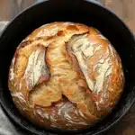Close-up of a golden-brown no knead bread in a cast iron dutch oven with a crisp crust.