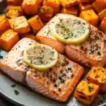 Close-up of sheet pan salmon with sweet potatoes and herbs on a clean background.