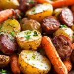 Close-up of sheet pan with sausage, potatoes, and carrots, showcasing vibrant colors and textures.