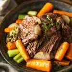 Close-up of a slow cooker beef chuck roast with rich, savory sauce and herbs.