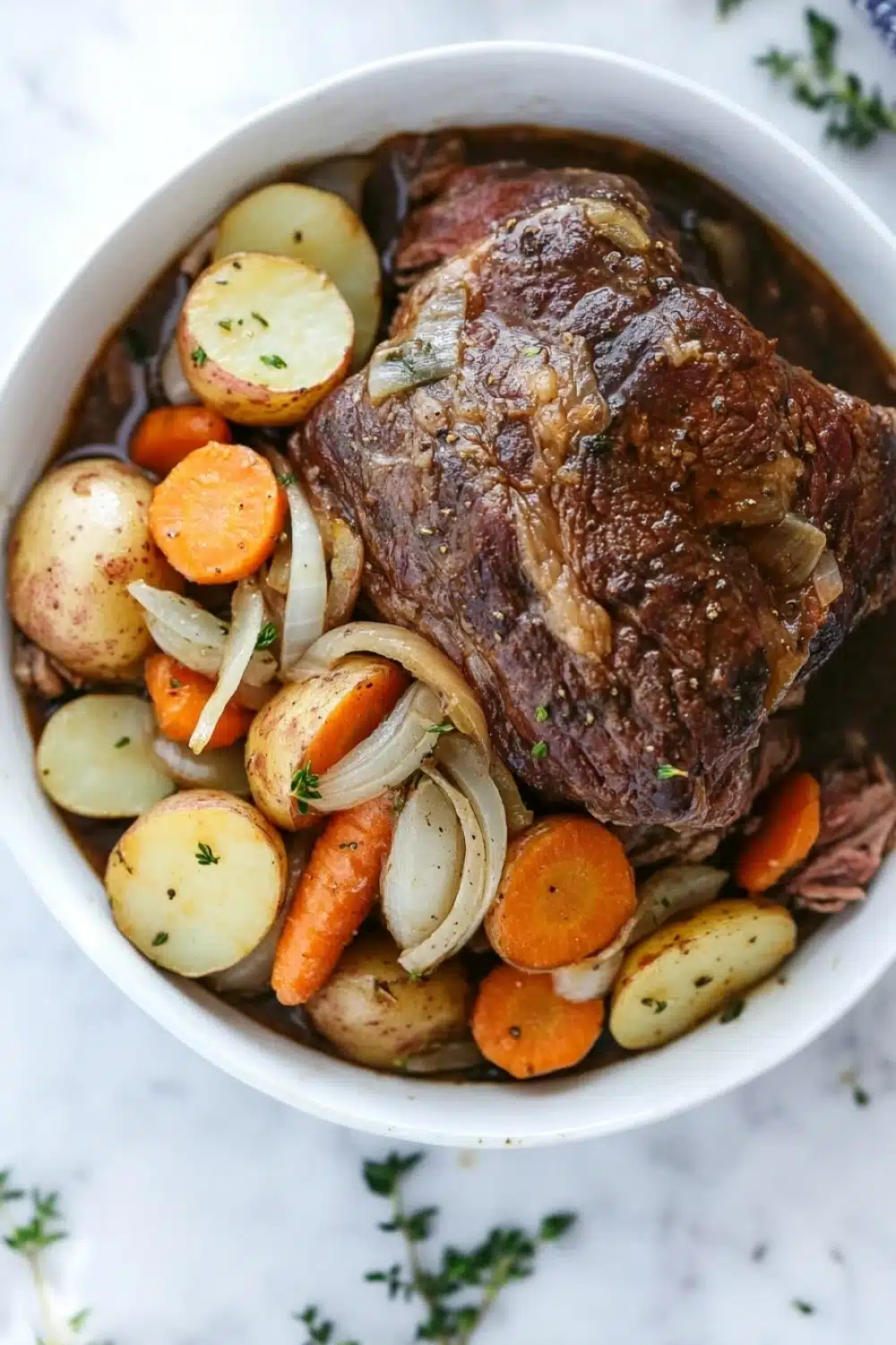 3 packet pot roast slow cooker - the image shows a large white bowl filled with a dish of beef stew. the beef appears to be cooked medium-rare and has a rich, dark brown color. it is garnished with sliced onions, carrots, and potatoes. the dish is served on a white marble countertop with a blue and white striped napkin on the side. there are also some sprigs of parsley scattered around the bowl. the overall appearance of the dish is hearty and appetizing.