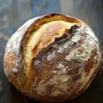 Bread with self rising flour - the image is a close-up of a freshly baked loaf of bread on a wooden surface. the bread appears to be freshly baked, with a golden brown crust and a soft, fluffy interior. the edges of the bread are slightly curled, indicating that it has been freshly baked. the loaf is resting on a dark, textured surface, possibly a table or countertop. the background is blurred, making the bread the focal point of the image.