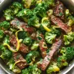 Lemon garlic butter steak and broccoli skillet - the image shows a large stainless steel skillet filled with cooked beef and broccoli. the beef appears to be medium-rare and has a pinkish-brown color. the broccoli is bright green and looks fresh and healthy. the skillet is sitting on a wooden cutting board with a white cloth napkin on the side. there are also some chopped herbs scattered around the skillet. the overall appearance of the dish is savory and appetizing.