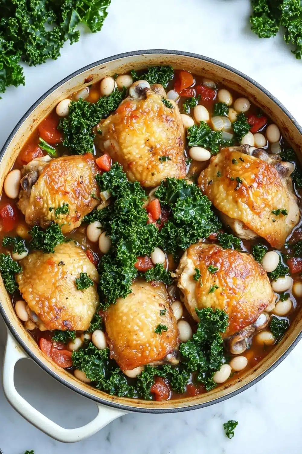 One pot braised chicken with kale and white beans - the image shows a large white ceramic pot filled with a dish of chicken and white beans. the dish appears to be a stew or stew with chunks of chicken, white beans, and kale. the chicken is golden brown and looks crispy on the outside. the white beans are white and appear to be cooked until they are soft and fluffy. the kale is bright green and looks fresh and vibrant. the pot is sitting on a white marble countertop with a few sprigs of parsley scattered around it.