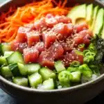 Tuna poke bowl cooked - the image is a close-up of a bowl of food. the bowl is made of dark brown ceramic and is placed on a black countertop. the food in the bowl appears to be a salad with various ingredients. on top of the salad, there are sliced cucumbers, sliced carrots, sliced avocado, and green onions. the vegetables are arranged in a colorful and appetizing manner. there are also sesame seeds sprinkled on top, adding a crunchy texture to the dish. the background is blurred, making the bowl the focal point of the image.