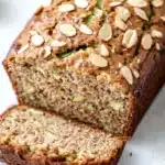 Zucchini bread almond flour - the image shows a loaf of bread with a golden brown crust and a soft, fluffy interior. the bread is topped with sliced almonds, giving it a crunchy texture. the slices are arranged in a way that they are overlapping each other, creating a layered effect. the background is white, making the bread stand out. the overall color scheme of the image is warm and inviting, with the bread being the main focus.
